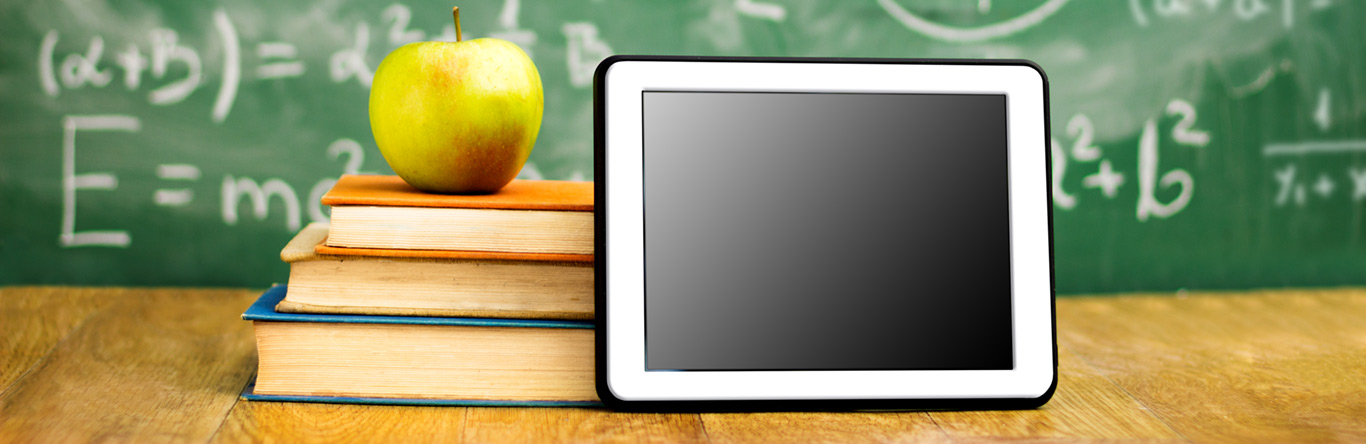 green apple on 3 books next to tablet in front of chalk board